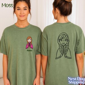 A young woman wearing a green t-shirt with a cartoon character printed on the front and a graphic of a girl on the back.