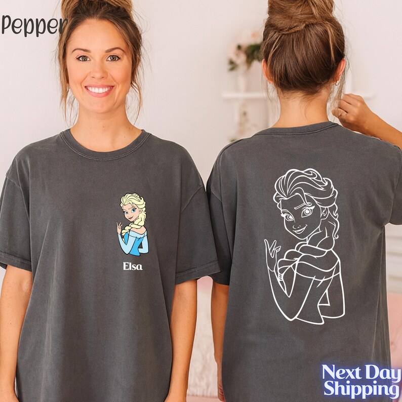 A woman wearing a gray t-shirt with a cartoon character printed on it, smiling at the camera.