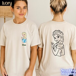 A woman wearing a white t-shirt with a cartoon image of a blonde woman on the front and a black and white line drawing of a woman on the back.