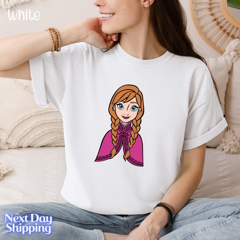 A woman wearing a white t-shirt with a cartoon illustration of a young girl with braided hair.