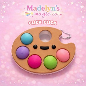 May include: A wooden-colored, palette-shaped toy with colorful, circular push bubbles. The toy has a smiley face design and the text "CLICK CLICK" is visible. The background is pink with stars and the text "Madelyn's magic co."