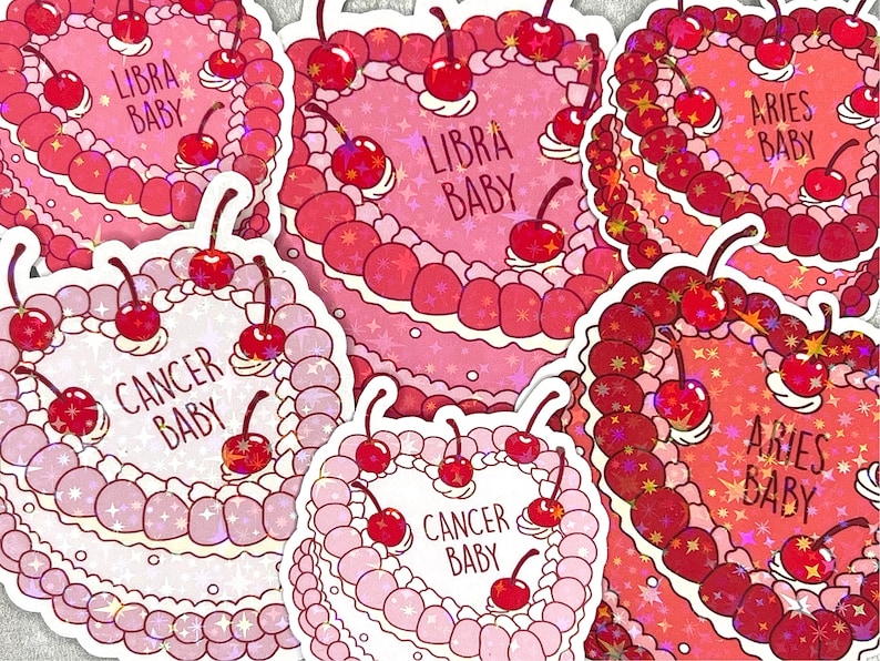 May include: Six pink and white heart-shaped cakes with glitter and cherries. Each cake has a different zodiac sign written on it: Libra Baby, Cancer Baby, Aries Baby.