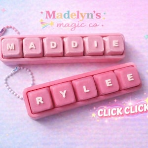 May include: Two pink keyboard-shaped name tags, one spelling "MADDIE" and the other "RYLEE", with white letters. The tags are on a pastel background with the text "Madelyn's magic co." and "CLICK CLICK".