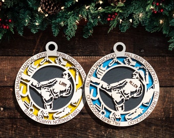 May include: Two round wooden ornaments featuring a silhouette of a person performing a martial arts kick. The ornaments are decorated with yellow and blue paint and the text "Twin Dragon Martial Arts" and "Fall River Taekwondo-Do". The names "Liam" and "Allen" are written on the ornaments.