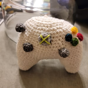 May include: White crocheted plush toy shaped like a video game controller with colorful buttons.