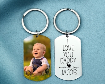 May include: A silver keychain with two tags. One tag has a photo of a baby boy and the other tag has the text "I love you daddy Jacob" with an arrow and a heart.
