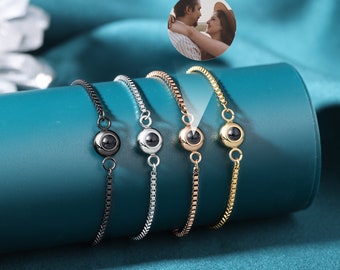 May include: Four silver bracelets with a small round charm that projects an image when viewed from a specific angle. The charms are black, silver, rose gold, and gold.