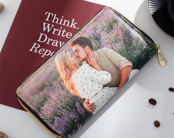 Puede incluir: Una cartera personalizada con una imagen romántica de una pareja en un campo de lavanda. La cartera tiene una cremallera dorada y un interior negro. El texto "Think. Write. Draw. Report." es visible sobre un fondo granate.