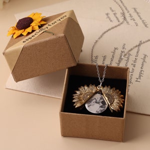 Può includere: Una collana con un ciondolo a forma di girasole dorato che contiene una foto, presentata in una scatola regalo marrone con un motivo a girasole e il testo "especially for you".