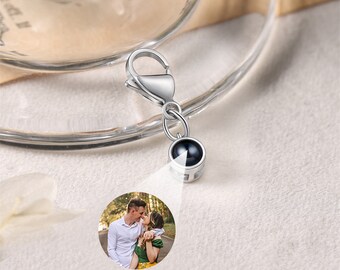 May include: Silver charm with a small black bead that can be used to hold a photo. The bead has a silver frame around it. The charm has a lobster clasp.
