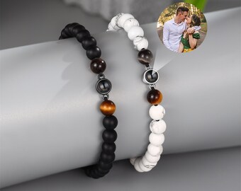 May include: Two beaded bracelets with a hidden photo charm. One bracelet is black with brown beads and the other is white with brown beads.