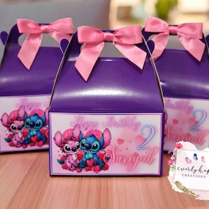 May include: Three purple gable boxes with pink satin bows on top. Each box features a graphic of Stitch and Angel surrounded by red hearts and roses. The text reads Happy Birthday 2 Sariyah in a pink script font against a soft pink background.