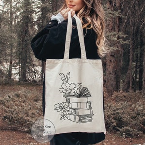 May include: A white canvas tote bag with black line art of a stack of books and flowers. The text "Large Size and Jumbo Size Tote Bags" is printed on the bottom of the bag.