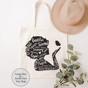 May include: A white canvas tote bag with black text and a silhouette of a woman's head. The text includes words like "strong", "beautiful", "talented", "inspiring", "confident", "happy", "magical", "ambitious", and "independent". The bag has the text "Large Size and Jumbo Size Tote Bags" at the bottom.