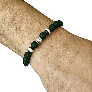 May include: A black beaded bracelet with white and silver accents. The bracelet features dark green, round beads, interspersed with white and black beads, and a silver-coloured spacer bead. The bracelet is worn on a wrist.