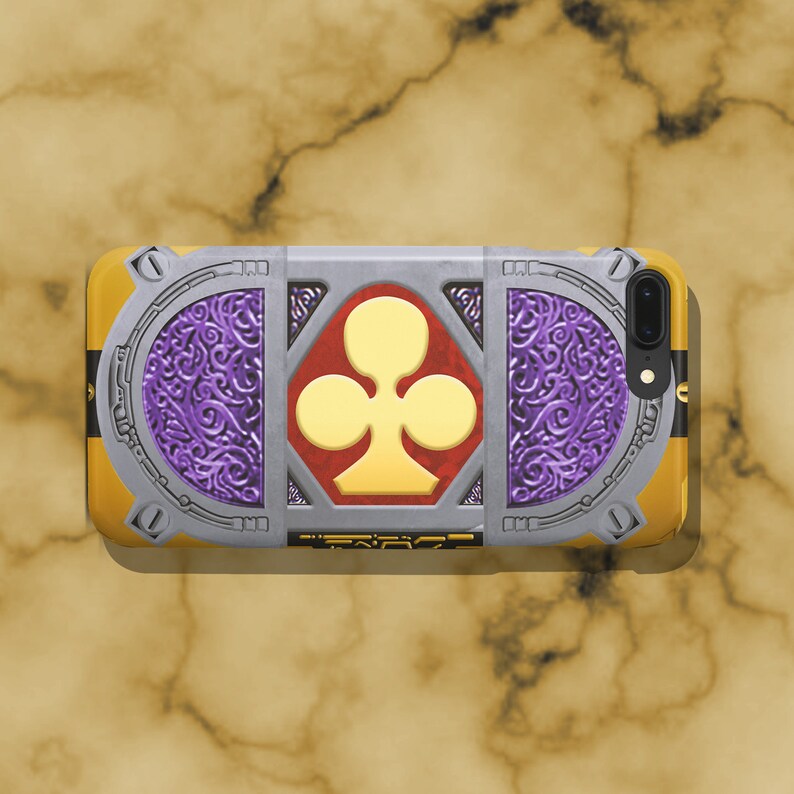 May include: A phone case with a gold and silver design featuring a stylized clover in the center. The clover is yellow with a red outline. The case has a purple and silver patterned border.