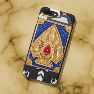 May include: A black phone case with a gold and blue design featuring a beetle with a red gem. The case has a black and white pattern on the bottom.