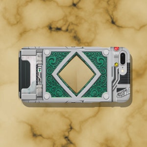 May include: A silver and green phone case with a decorative design. The case has a diamond-shaped cutout in the center and a small red button on the top right corner.
