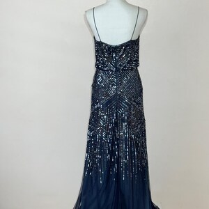 May include: A navy blue evening gown with a beaded bodice and a flowing skirt. The dress features thin spaghetti straps and a detailed sequin pattern. The skirt has a layered, sheer fabric.