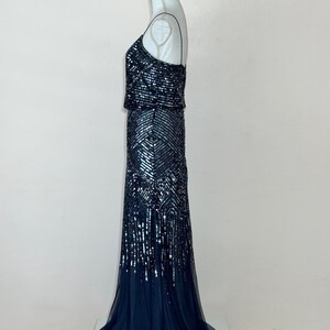 May include: A formal, floor-length gown with a dark blue sequined bodice and skirt. The dress features a fitted silhouette with a flowing, sheer train. The bodice has a square neckline and spaghetti straps.