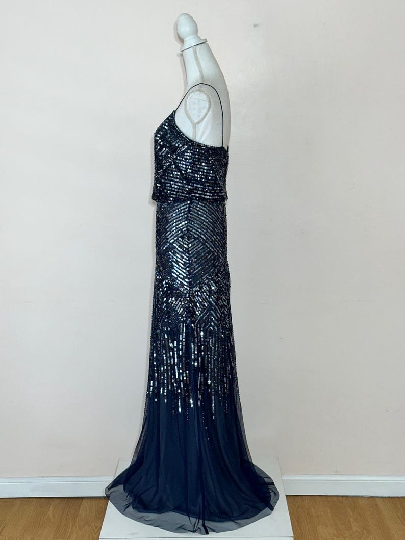 May include: A formal, floor-length gown with a dark blue sequined bodice and skirt. The dress features a fitted silhouette with a flowing, sheer train. The bodice has a square neckline and spaghetti straps.