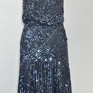 May include: A dark gray sequined dress with a V-neckline and spaghetti straps. The dress features a fitted bodice and a flowing skirt, with a geometric pattern of sequins. The dress is floor-length and suitable for formal events.