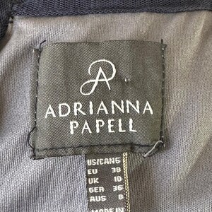 May include: Close-up of a dark gray fabric label with the brand name "ADRIANNA PAPELL" in white. The label includes size conversions for US/CAN, EU, UK, GER, and AUS. The tag also states "MADE IN INDIA".
