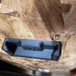May include: A black plastic wall mount with a rectangular shape and a small hole in the center.