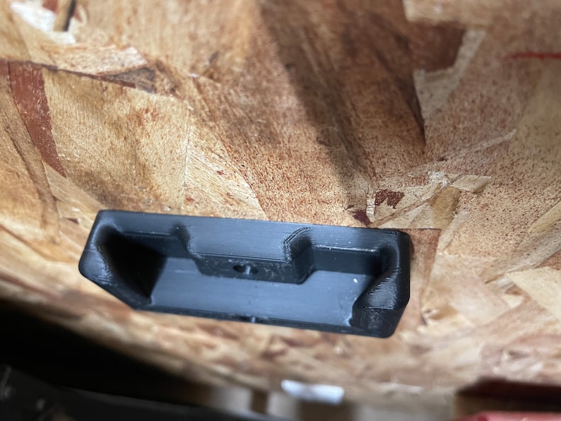 May include: A black plastic wall mount with a rectangular shape and a small hole in the center.