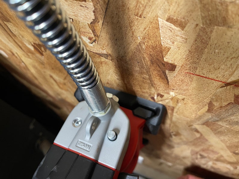 May include: A close-up of a red and silver power tool with a flexible hose attached. The tool is mounted to a wooden surface.