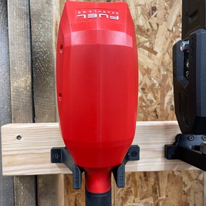 Puede incluir: Una herramienta eléctrica inalámbrica roja y negra con el texto "FUEL BRUSHLESS" en el lateral. La herramienta está montada en una pared de madera.