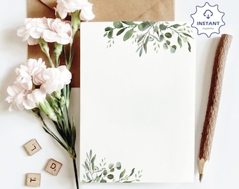 May include: A blank white card with a green leafy border. The card is sitting on a white surface with a brown envelope, a pencil, and some wooden letter tiles.