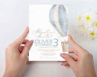 Puede incluir: Un globo aerostático azul y blanco con una cesta marrón. El texto "Adventure Awaits! Oliver is turning 3" está impreso en la invitación. La invitación es para una fiesta de cumpleaños.