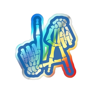 May include: A holographic sticker featuring a skeletal hand giving the 'one' sign, with the letters 'LA' in a skeleton hand design. The sticker has a gradient of blue, yellow, and red colors.