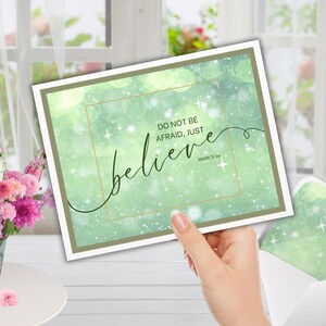 Może przedstawiać: Kartka okolicznościowa z zielonym tłem akwarelowym i napisem "DO NOT BE AFRAID, JUST believe" w eleganckiej czcionce. Kartka jest trzymana przed oknem z kwiatami i kopertą.