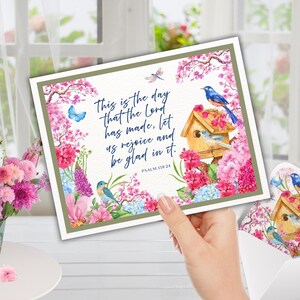 May include: A floral greeting card with the text "This is the day that the Lord has made, let us rejoice and be glad in it." The card features illustrations of birds, a birdhouse, flowers, and a butterfly. A matching card is in a white envelope.