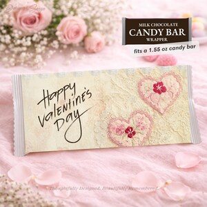Puede incluir: Envoltorio de barra de chocolate para el Día de San Valentín con un diseño de encaje crema y el texto "Happy Valentine's Day". Se presentan dos corazones bordados con detalles florales. El envoltorio se adapta a una barra de chocolate de 43,9 gramos.