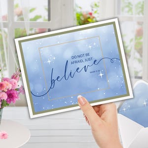Może przedstawiać: Kartka okolicznościowa z niebieskim tłem akwarelowym i napisem "Do not be afraid, just believe". Karta jest trzymana przed oknem z kwiatami.