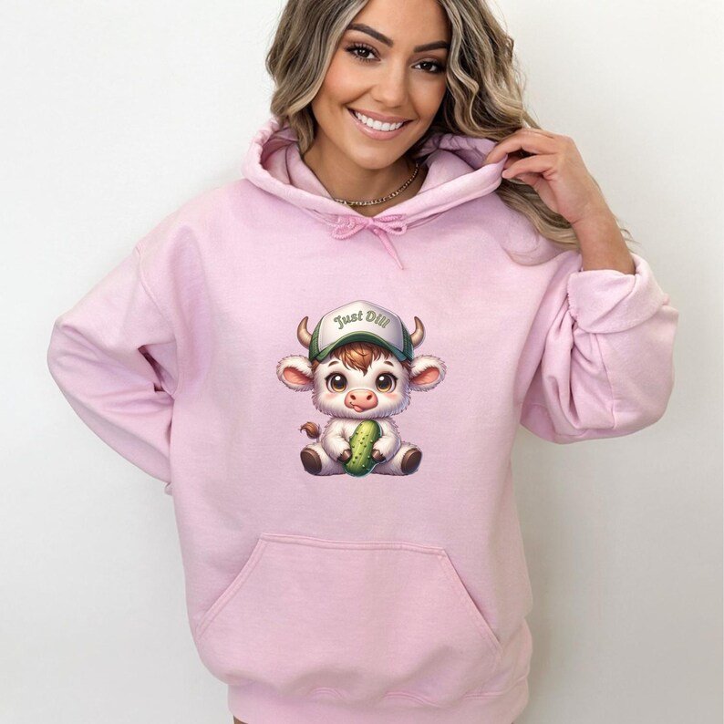 May include: Pink hoodie with a cartoon cow wearing a baseball cap that says "Just Dill" and holding a pickle.