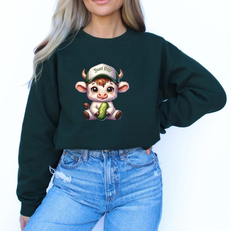 May include: A dark green cropped sweatshirt with a cartoon illustration of a white cow wearing a baseball cap that says "Just Dill" and holding a green pickle.