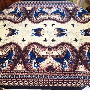 Può includere: Una tovaglia rotonda con sfondo bianco e un motivo ripetitivo di farfalle blu. Le farfalle sono contornate di nero e hanno un motivo marrone e bianco sulle ali. La tovaglia ha un bordo marrone e bianco con un motivo ripetitivo di piccole farfalle.