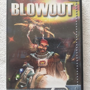 Puede incluir: Caja de juego para PC CD-ROM de "BLOWOUT" con una escena de acción futurista. La portada muestra un personaje con traje espacial empuñando un arma, un monstruo y el título del juego.