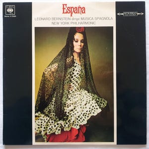 Op de afbeelding: Vintage vinyl albumhoes getiteld "España" met een vrouw in een polkadot jurk en zwarte kanten sjaal. Het album is van Leonard Bernstein en het New York Philharmonic. De hoes heeft een CBS-logo en de tekst "Stereo".