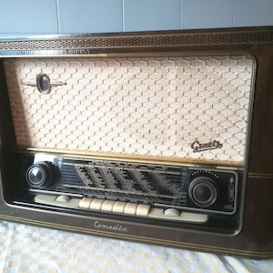 Könnte beinhalten: Ein vintage braunes Holzradio mit goldener Verzierung und einem Wabengitter-Lautsprechergitter. Das Radio hat ein schwarzes Zifferblatt mit silbernen Knöpfen und einem silbernen Typenschild mit der Aufschrift "Comedia" und "Graetz".