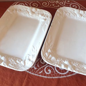 Könnte beinhalten: Zwei rechteckige Servierplatten aus weißer Keramik mit einem erhabenen Reliefdekor aus verschiedenen Früchten und Blättern. Die Platten haben eine glatte, flache Oberfläche in der Mitte und einen strukturierten, geformten Rand.
