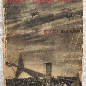 Op de afbeelding: Een vintage boekomslag met de titel "EROI DELL'ARIA" in rode letters. De omslag toont een zwart-wit afbeelding van vliegtuigen in de lucht en een verwoest gebouw.