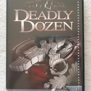 Peut inclure: Boîtier de jeu PC CD-ROM pour "Deadly Dozen" avec un design sombre et métallique. Le titre est en grandes lettres argentées. La couverture présente une illustration détaillée d'un aigle en pierre et d'autres éléments graphiques.