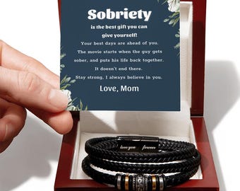 May include: A wooden box containing a blue card with the message "Sobriety is the best gift you can give yourself! Your best days are ahead of you. The movie starts when the guy gets sober, and puts his life back together. It doesn't end there. Stay strong, I always believe in you. Love, Mom". The box also contains a black leather bracelet with the words "love you forever" engraved on it.