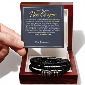 May include: A black braided leather bracelet with metallic beads in a polished wooden box. The box contains a card with the text: Here's To Your Next Chapter. You've worked so hard to make your dreams come true, and no one deserves this more than you!