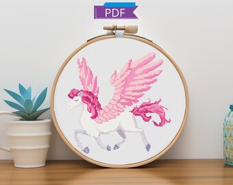 May include: A cross-stitch pattern of a pink winged unicorn in a wooden embroidery hoop. The unicorn is white with pink wings, mane, and tail.